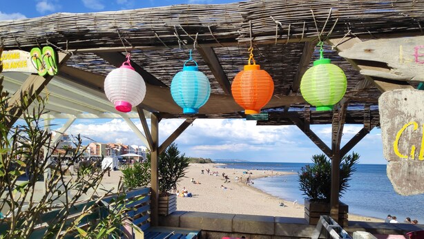 A beachside café with wooden furniture and hanging paper lanterns. - CAP D'agde, Agréable 2 Pièces 42m2, Loggia, 4 Voyageurs, 300m Plage du Môle (Agde)