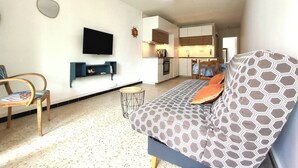 A living room with a sofa, a TV, a small table, and a chair. - CAP D'agde, Agréable 2 Pièces 42m2, Loggia, 4 Voyageurs, 300m Plage du Môle (Agde)