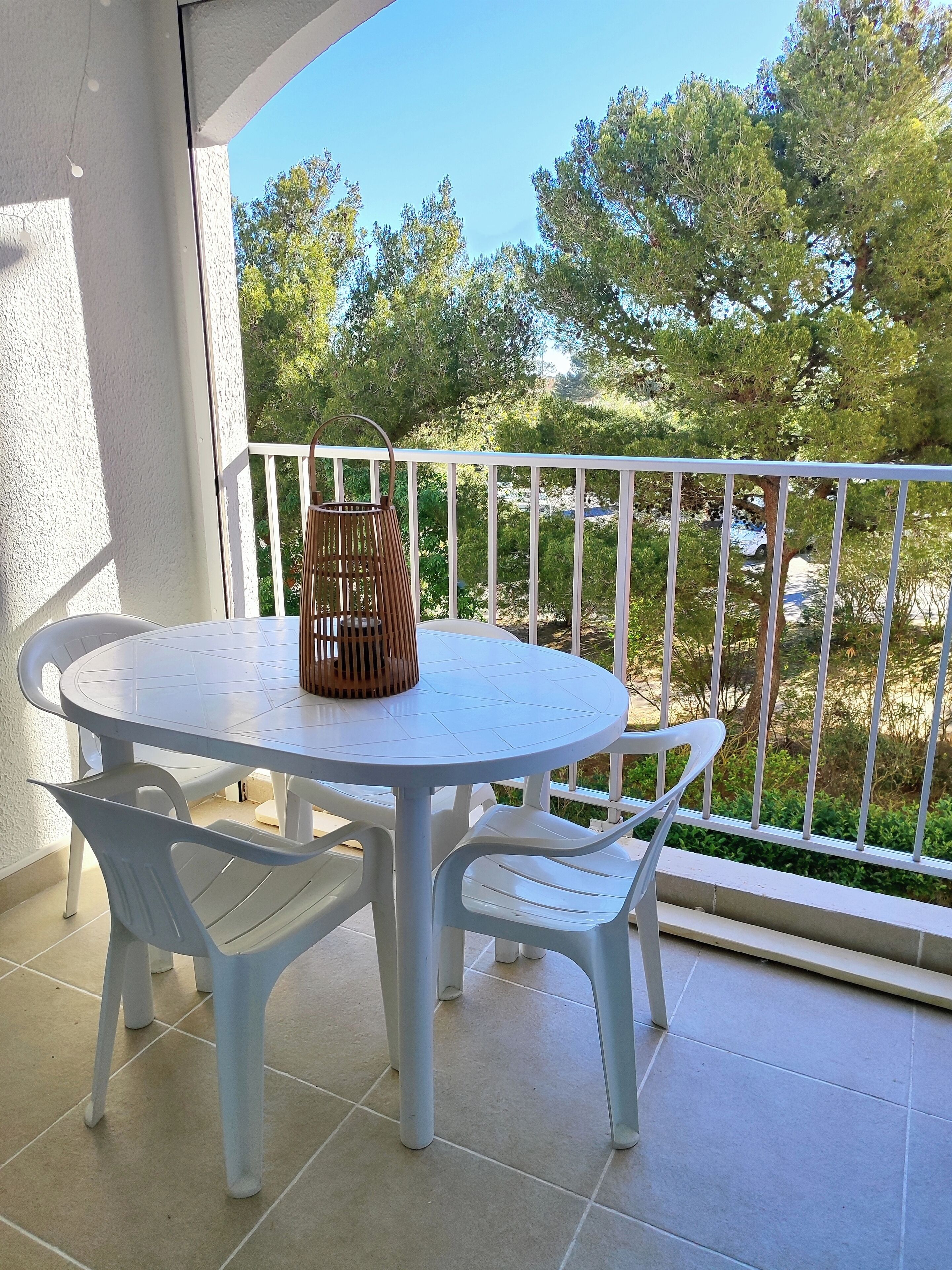 A round table with white chairs and a wicker basket on a balcony with white railings.