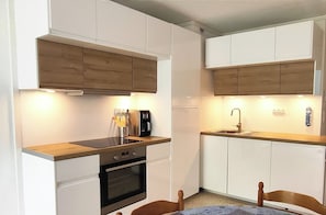 A compact kitchen with white cabinets, a wooden countertop, a coffee maker, and a sink.