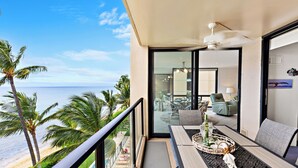 Ein Balkon mit Blick auf Strand und Meer, ein Esstisch mit Stühlen und ein Deckenventilator.