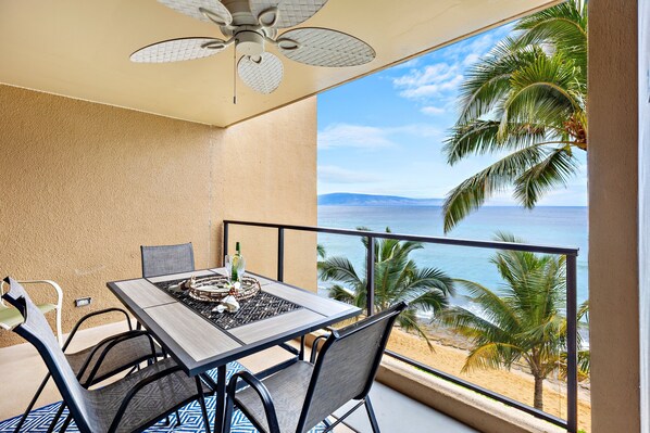 Varanda com mesa e cadeiras, com vista para uma praia e oceano.