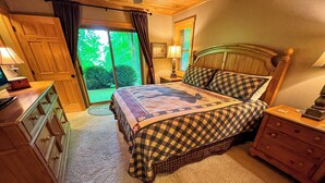 A bedroom with a large bed, wooden headboard, a nightstand, a dresser, and a view of a green outdoor area through a sliding door. - Bearly Behaving | 3BR Cabin w/ Hot Tub, Pool Table, Fire Pit (Todd)