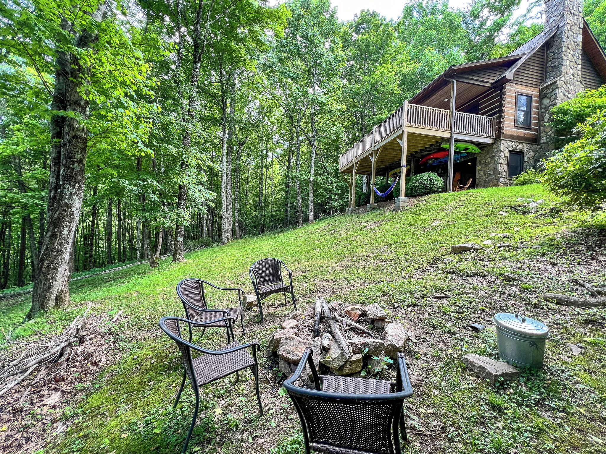 Une cabane dotée d’un porche couvert, entourée d’une forêt. On y trouve des chaises d’extérieur et un foyer.