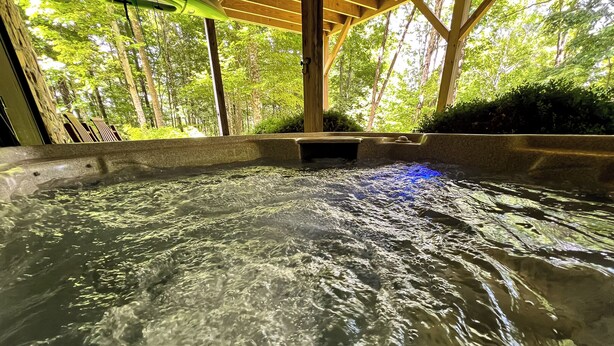 A hot spring area with clear water, surrounded by wooden structures and greenery. - Bearly Behaving | 3BR Cabin w/ Hot Tub, Pool Table, Fire Pit (Todd)