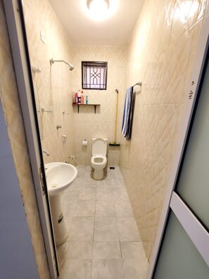 Een kleine badkamer met toilet, bidet en wastafel. Er is een raam met tralies, een handdoekhouder en een bezem die tegen de muur staat.