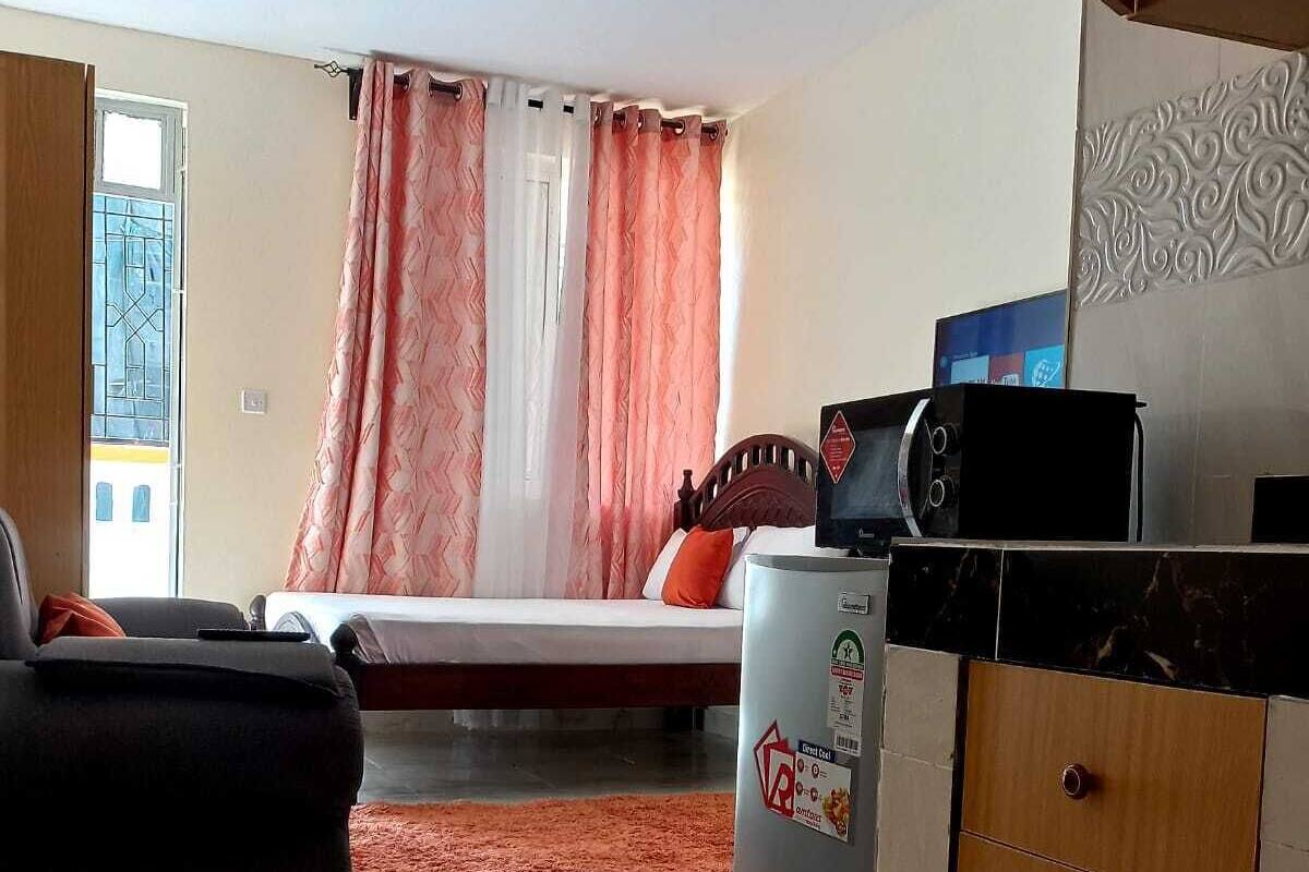 Een knus woongedeelte met een bed, kitchenette en een plafondventilator.