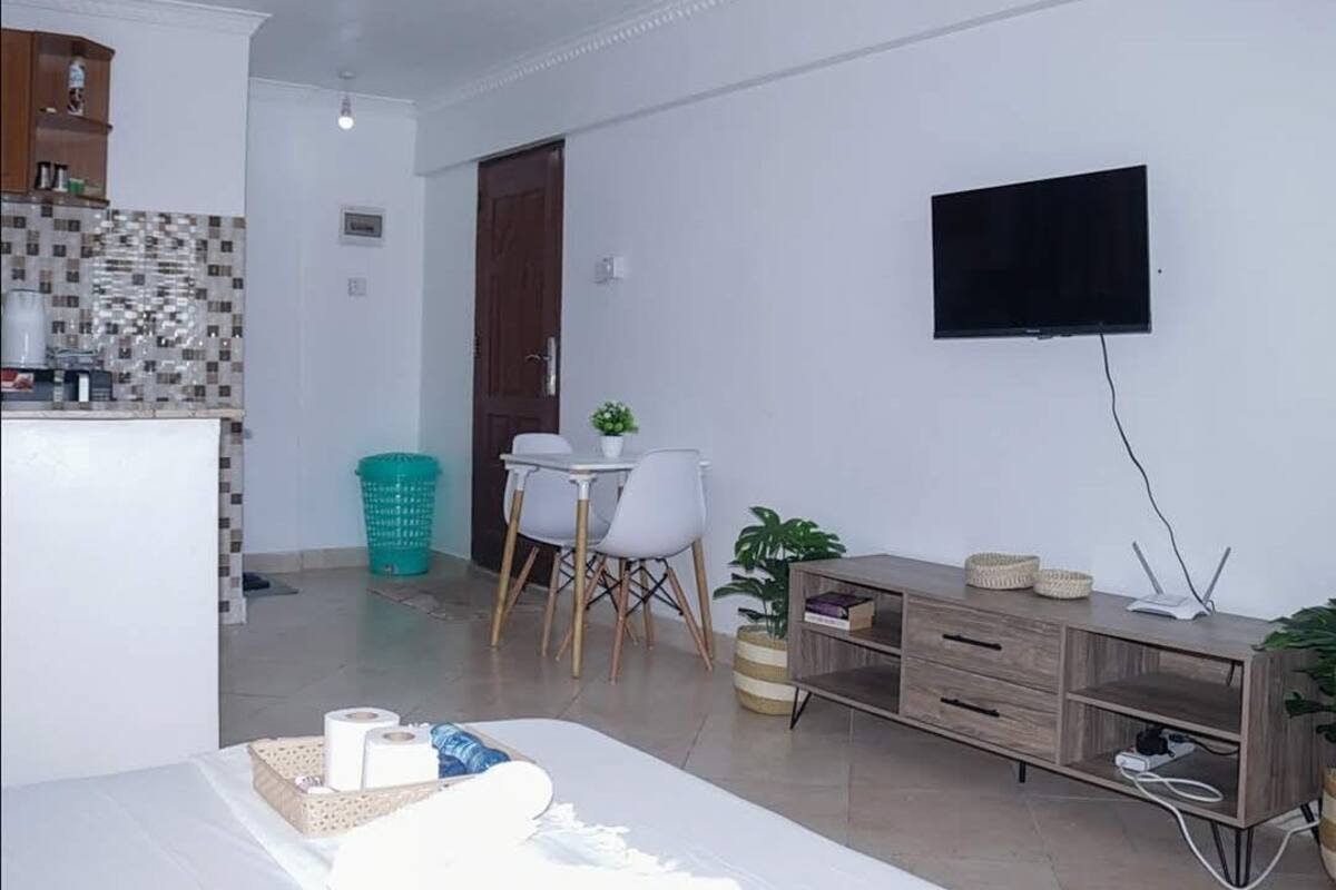 Een compacte leefruimte met een kitchenette, een eethoek en een aan de muur bevestigde televisie.