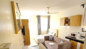 Een ruimtelijk ingerichte leefruimte met een kitchenette, een bank, een eettafel en een plafondventilator.