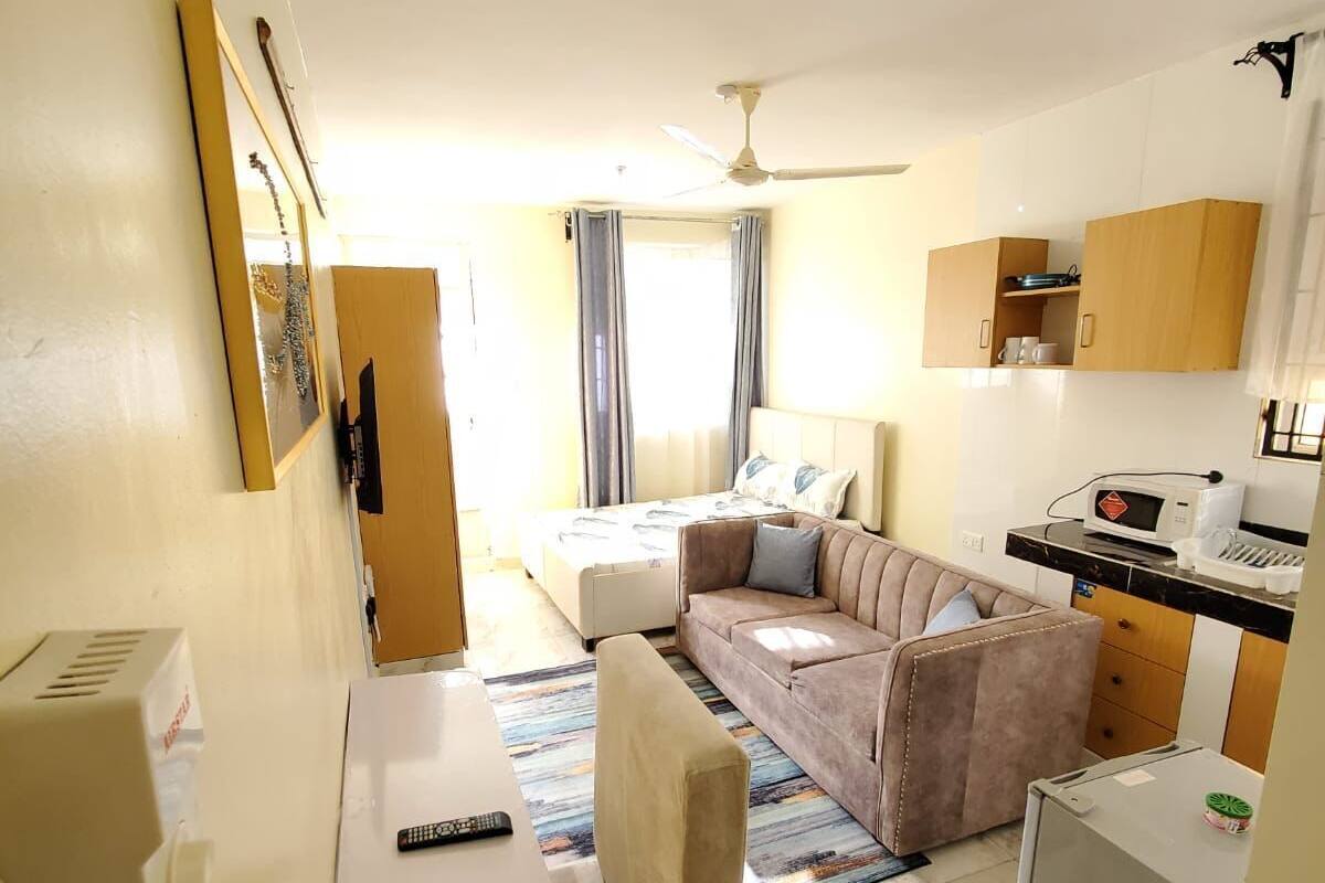 Een ruimtelijk ingerichte leefruimte met een kitchenette, een bank, een eettafel en een plafondventilator.
