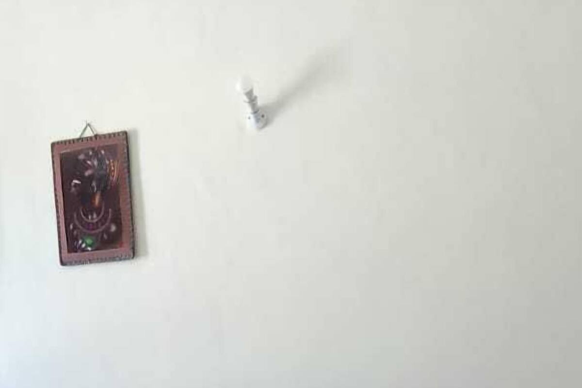 Een woonkamer met een bruine bank, een glazen salontafel met bladmotief en een witte muur met een fotolijst.