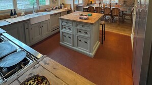 A spacious kitchen with a central island, large windows, and a dining area with wooden chairs.