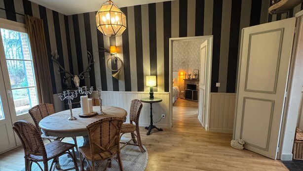 A dining area with a round table and wicker chairs, a chandelier, and a striped wall.