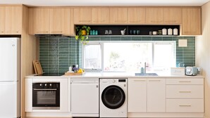 A compact kitchen with wooden cabinets, a built-in oven, a washing machine, and a window with a view of the outdoors.
