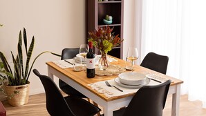 A dining area with a wooden table, black chairs, a wine bottle, and a potted plant.