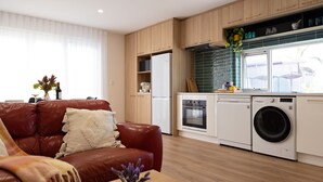 A modern kitchen with a built-in washing machine and oven, a red leather sofa, and a dining area with a vase of flowers.
