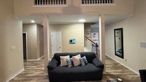 A spacious living area with a black sofa, wooden flooring, and a view of a bedroom with a staircase. - Cottage near the beach , owa, Bucees , King bed , WiFi quiet neighborhood  (Loxley)