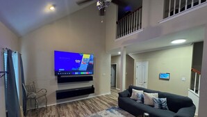 A modern living room with a flat-screen TV, a black sofa, a glass coffee table, and a staircase leading to an upper level. - Cottage near the beach , owa, Bucees , King bed , WiFi quiet neighborhood  (Loxley)