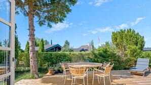 An outdoor wooden deck with a round table and chairs, surrounded by greenery and a clear sky. - "Synnöve" - 350m from the sea by Interhome (Væggerløse)