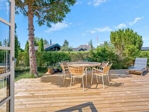 An outdoor wooden deck with a round table and chairs, surrounded by greenery and a clear sky. - "Synnöve" - 350m from the sea by Interhome (Væggerløse)