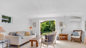 A modern living room with a sofa, a dining table, a wicker chair, and a view of a garden. - "Synnöve" - 350m from the sea by Interhome (Væggerløse)