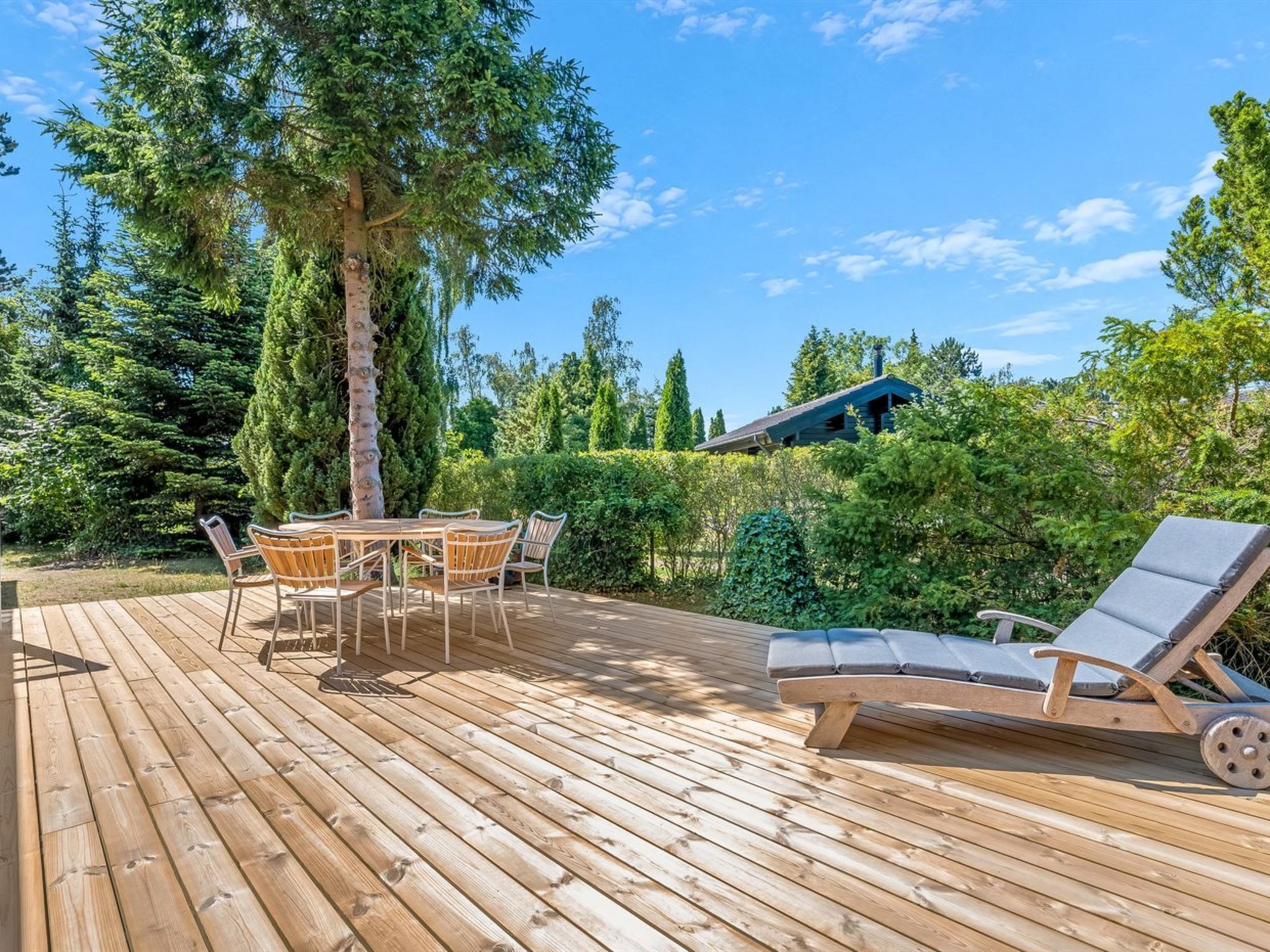 Une terrasse en bois avec une table et des chaises, un fauteuil de relaxation et un bâtiment en arrière-plan.