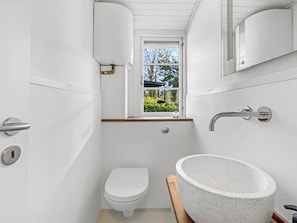Ein kleines Badezimmer mit Toilette, einem großzügigen Waschbecken und einem Fenster mit Blick auf Grünflächen.