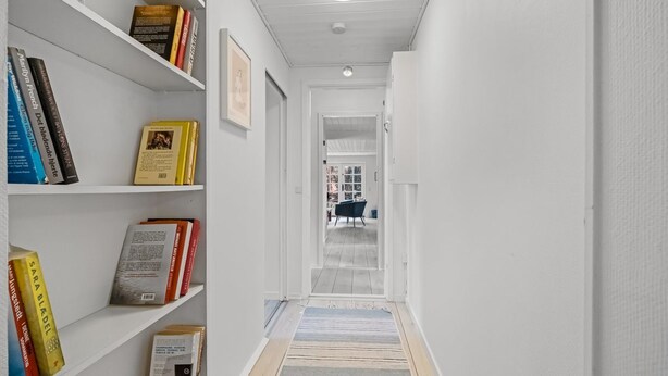 A narrow hallway with white walls, a wooden floor, and a bookshelf filled with books. - "Synnöve" - 350m from the sea by Interhome (Væggerløse)