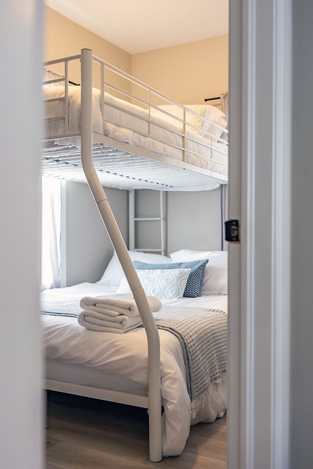 Una cama litera con escalera, una mesita de noche y una ventana con cortinas.
