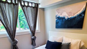 Un dormitorio con una cama grande, una ventana con cortinas, un cuadro en la pared y suelo de madera.