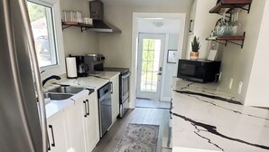 Una cocina moderna con armarios blancos, un refrigerador de acero inoxidable, una cafetera y una pequeña mesa con un tapete.