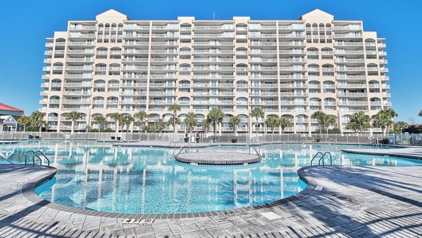 Un grand hôtel doté de nombreux balcons et d’un espace piscine central agrémenté d’un jacuzzi circulaire.