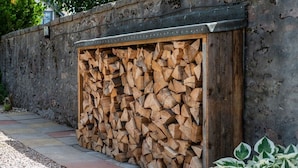 A stack of firewood against a stone wall, with a gravel path and a plant in the foreground. - Dormie Cottage, spacious bungalow with log fire! (Aberdeenshire)