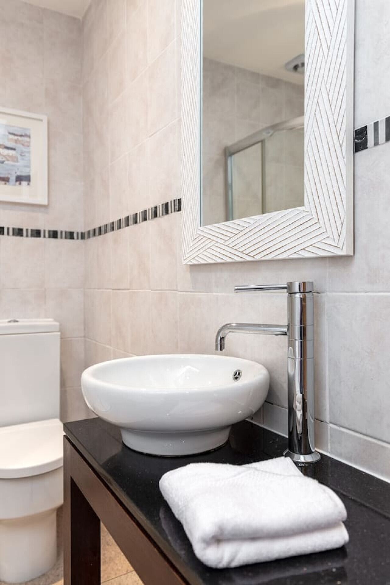 A modern bathroom with a white sink, chrome faucet, and a large mirror with a geometric frame.