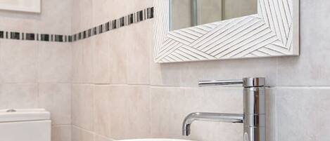 A modern bathroom with a white sink, chrome faucet, and a large mirror with a geometric frame.