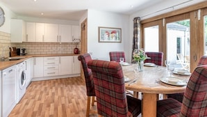 A kitchen with white cabinets, a wooden countertop, and a dining area with plaid chairs and a wooden table. - Dormie Cottage, spacious bungalow with log fire! (Aberdeenshire)