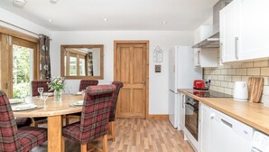 A dining area with a wooden table and plaid chairs, a kitchen with white cabinets and appliances, and a wooden door. - Dormie Cottage, spacious bungalow with log fire! (Aberdeenshire)