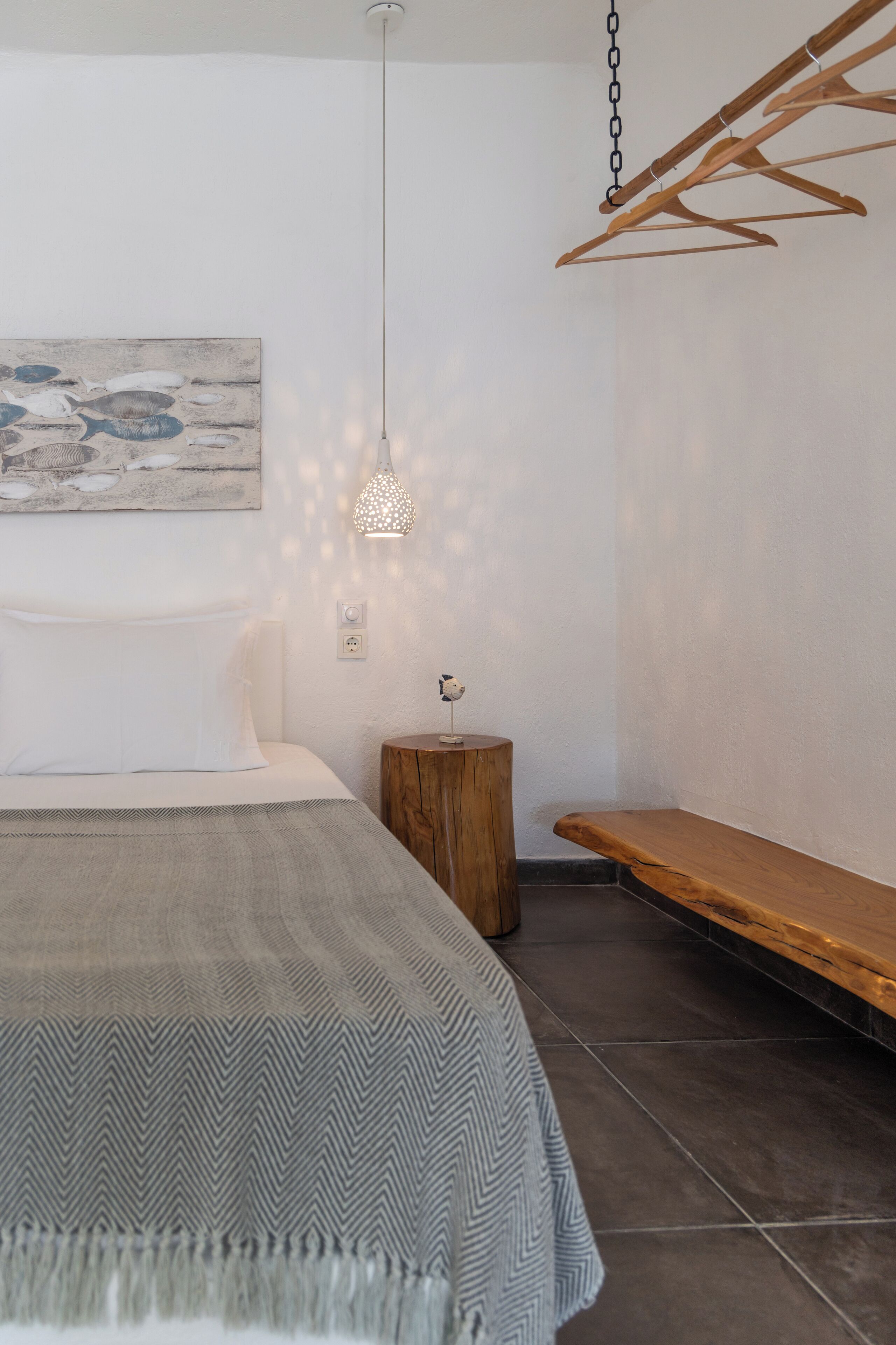 A bedroom with a bed, a hanging light fixture, a wooden bench, and a wall-mounted artwork.