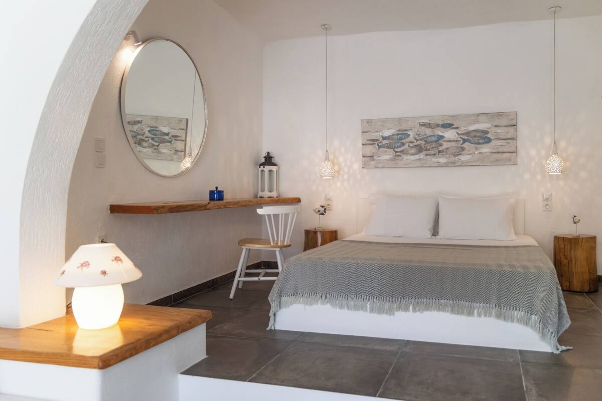 A bedroom with a bed, a chair, a nightstand, a lamp, a mirror, and artwork on the wall.