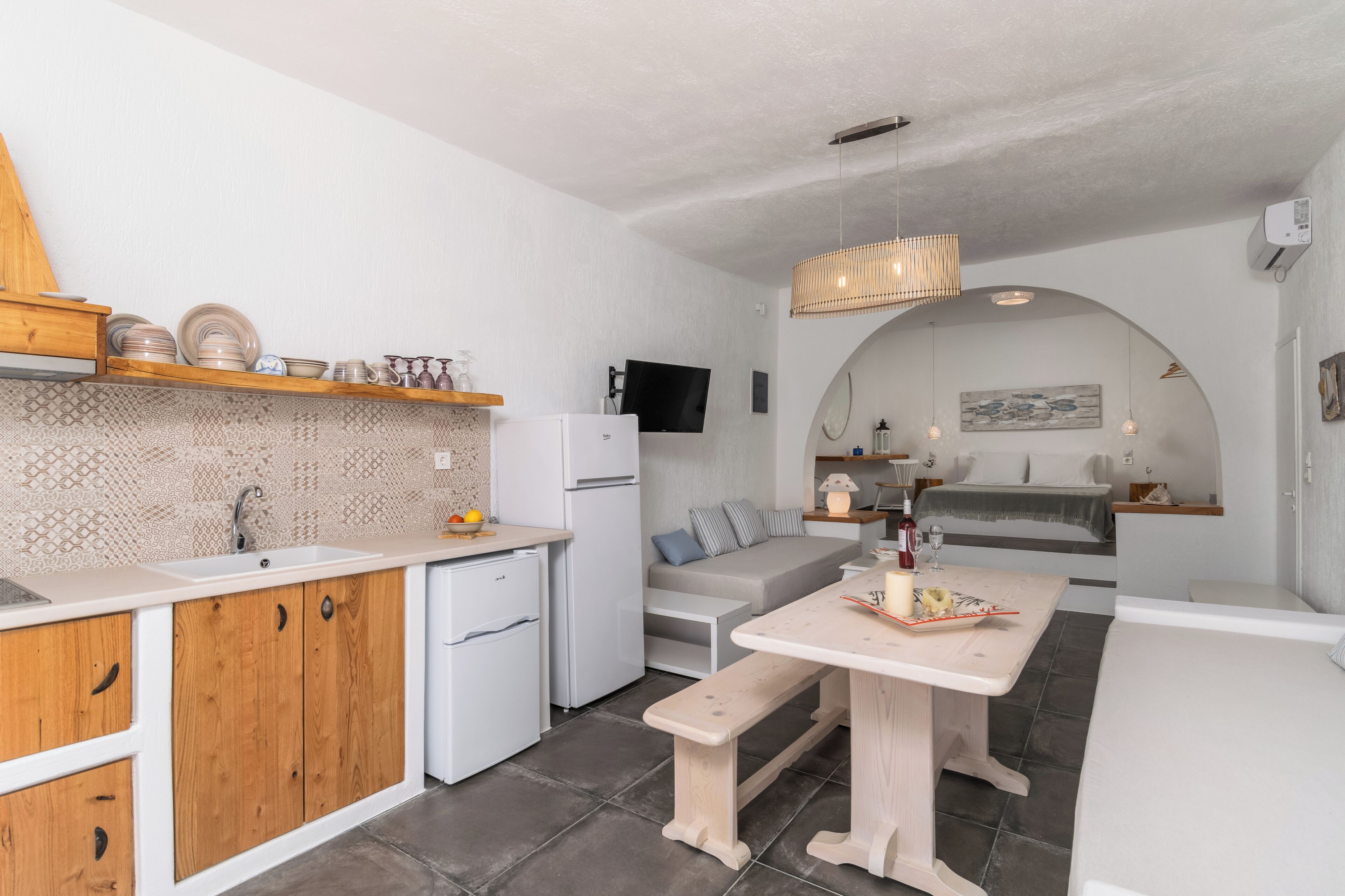 Eine kleine Küche mit Holzschränken, einem weißen Kühlschrank und einem Essbereich mit einer Bank.