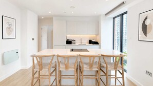 Une cuisine moderne avec des meubles blancs, un îlot central et un coin repas doté de chaises en bois.