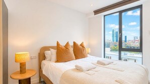 Une chambre d’hôtel avec un grand lit, deux lampes de chevet, une vue sur la ville à travers une grande fenêtre et un panorama urbain visible à l’extérieur.