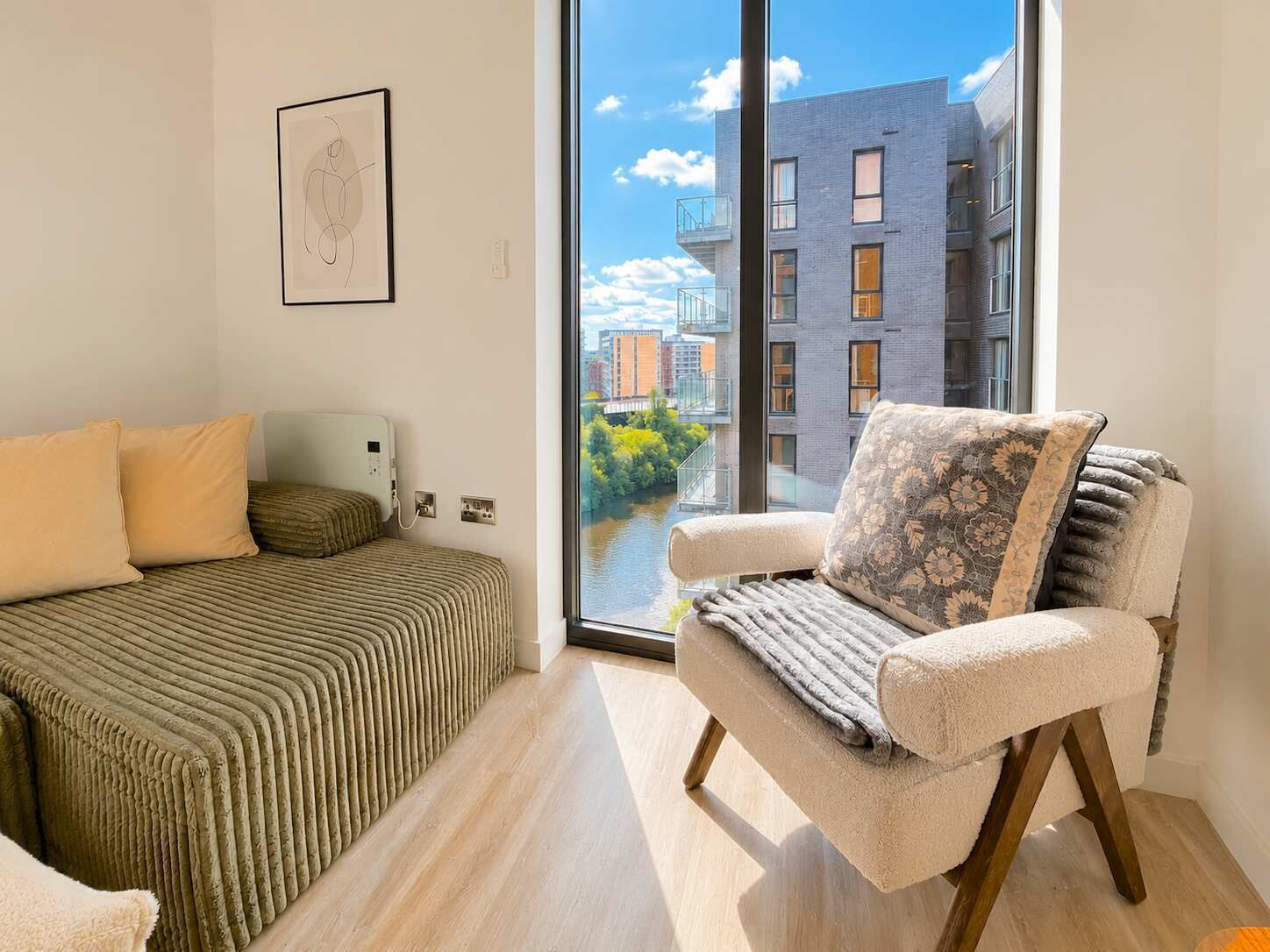 Ein modernes Schlafzimmer mit einem Bett, einem Sessel, einem Fenster und Blick auf ein Gebäude.