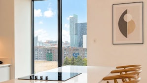 Une chambre moderne avec une grande fenêtre, une table blanche et une œuvre d’art abstraite encadrée.