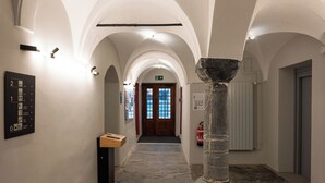 Un pasillo con techos abovedados, una columna de piedra, un banco de madera y una puerta al final.