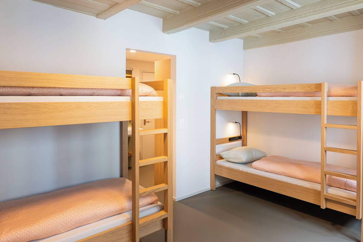 A room with bunk beds, wooden shelves, and a desk with a lamp.