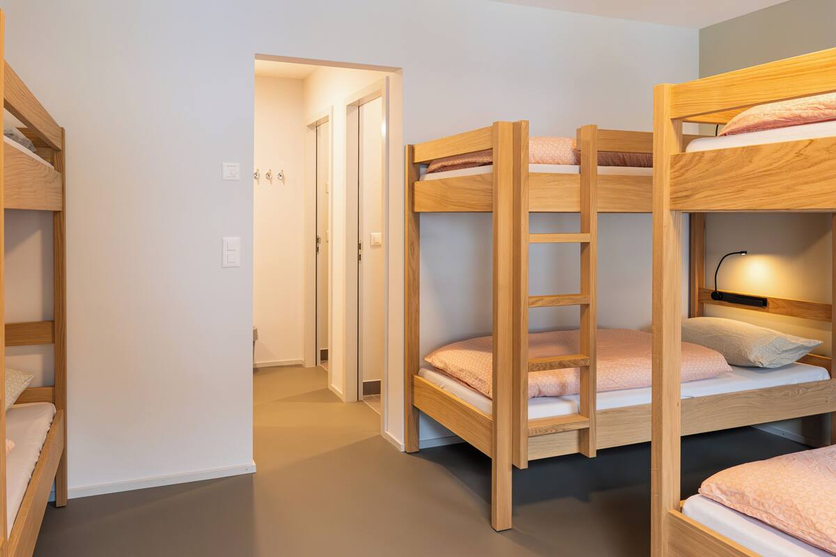 A bunk bed room with a ladder, wooden walls, and a door leading to another room.