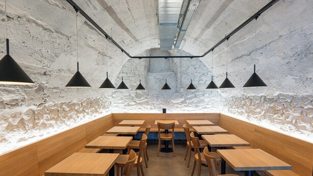 Un restaurante con paredes interiores de piedra rústica, mesas y sillas de madera, e iluminación colgante.