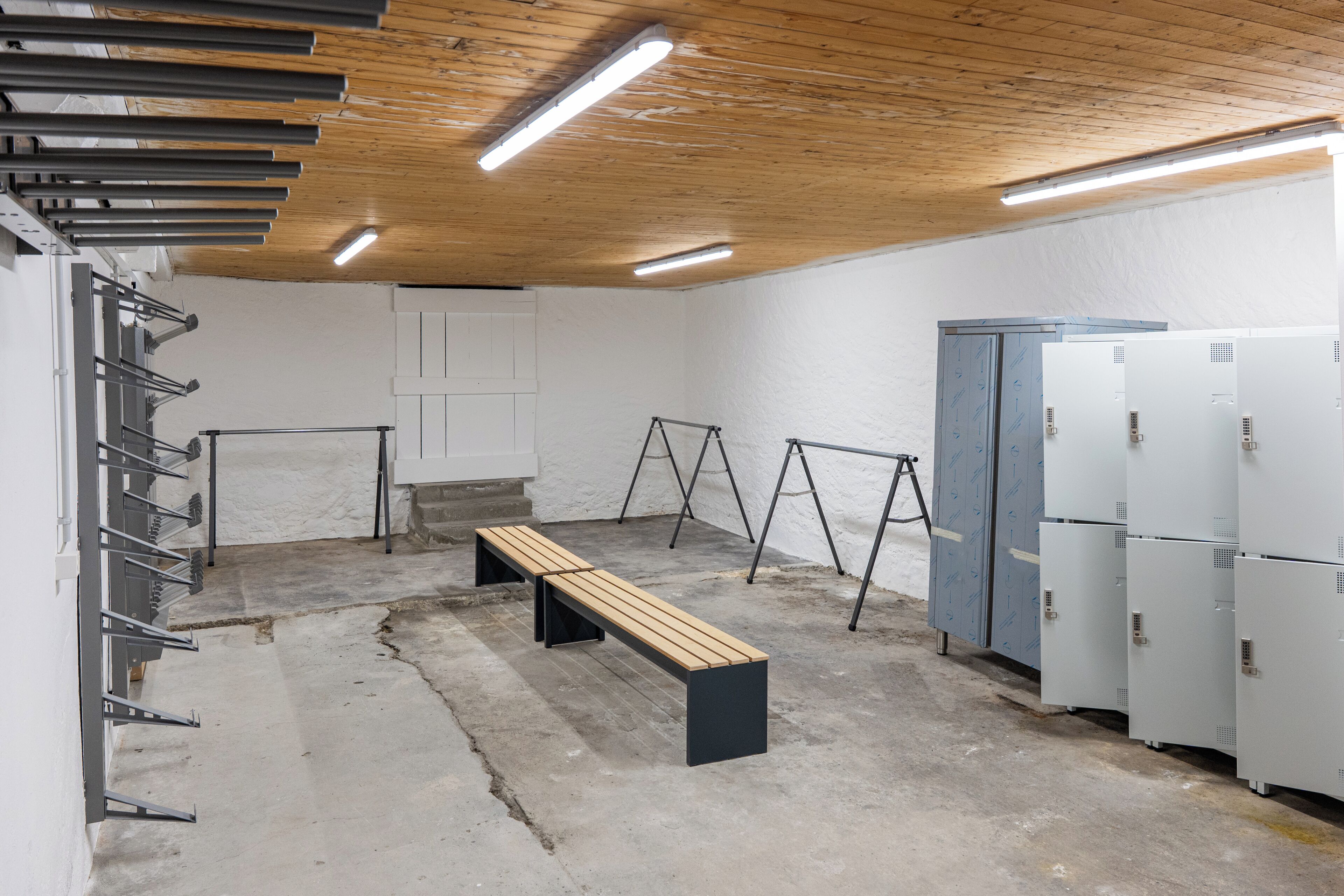 A gym with a wooden ceiling, concrete floor, a bench, exercise equipment, and lockers.