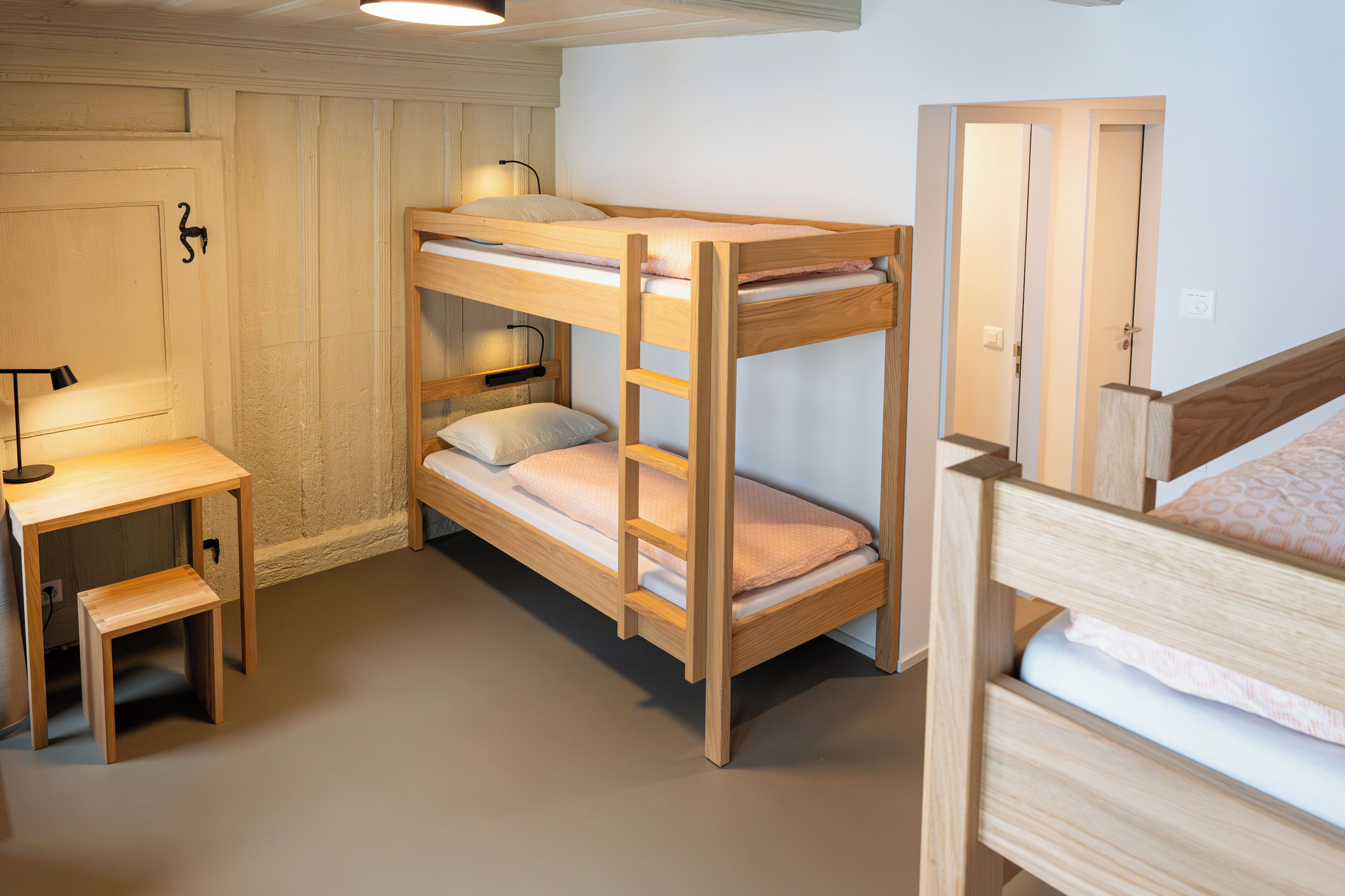 Une chambre avec un lit superposé, un bureau et une chaise, une porte et un luminaire.